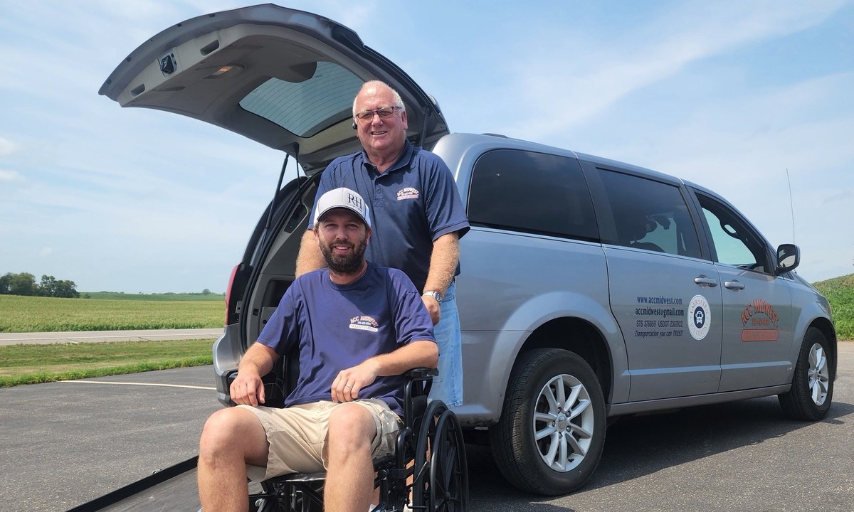 Driver with a client in a wheelchair beside an ACC Midwest van